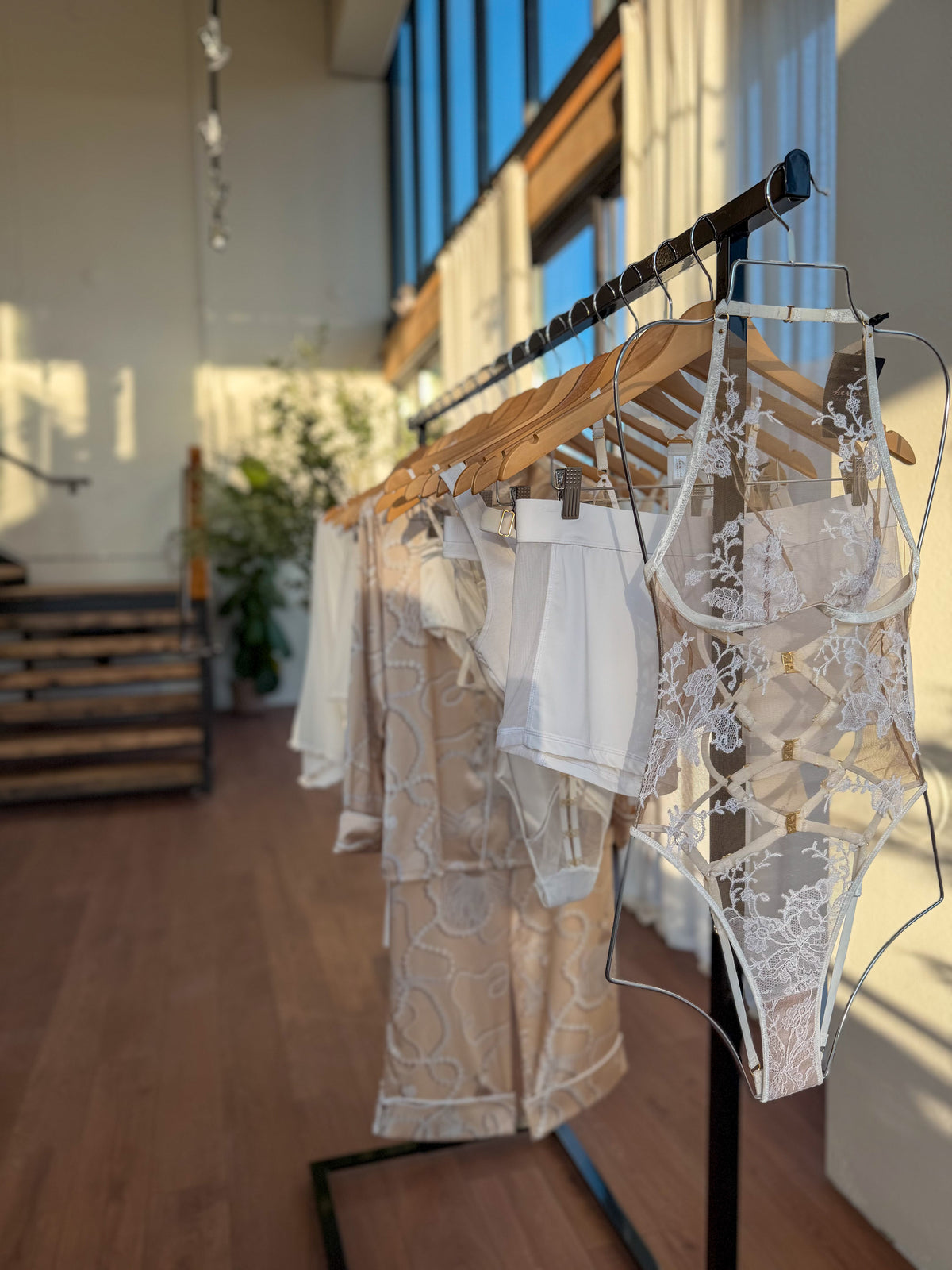 White lace bodysuit hanging on a rail of bridal lingerie and pajamas in natural light