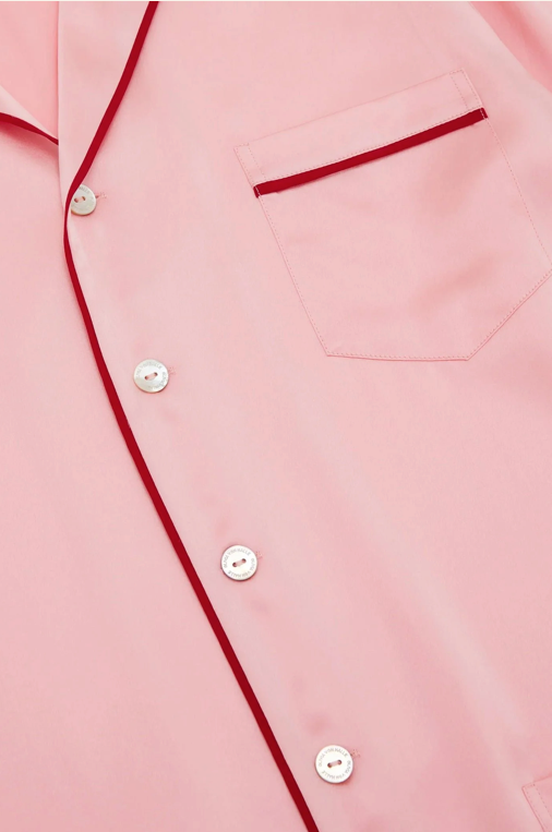 Close-up of a light pink button-up shirt with contrasting dark red piping along the placket and pocket edge, plus white buttons.